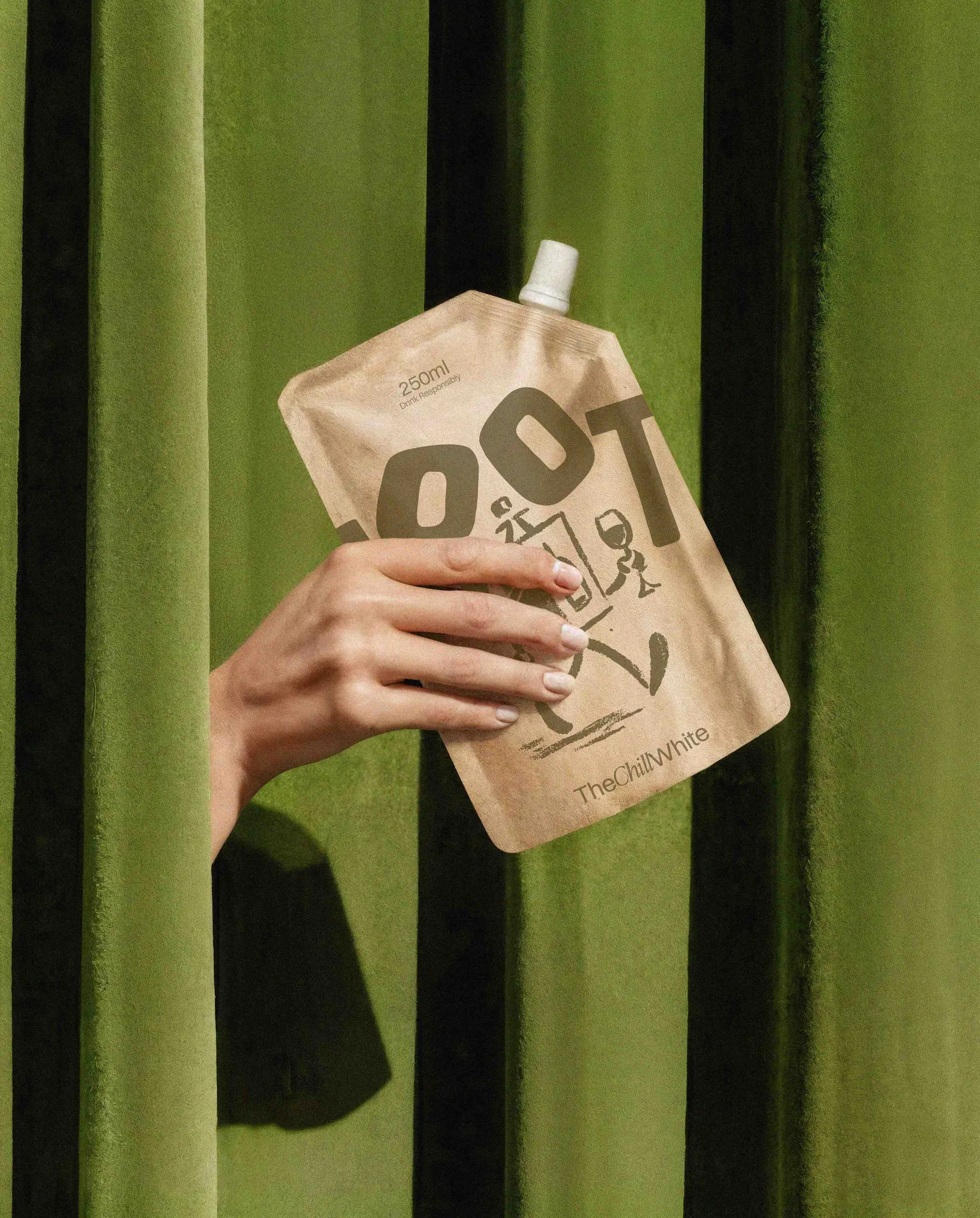 A hand holding a WOOT kraft pouch through olive green curtains