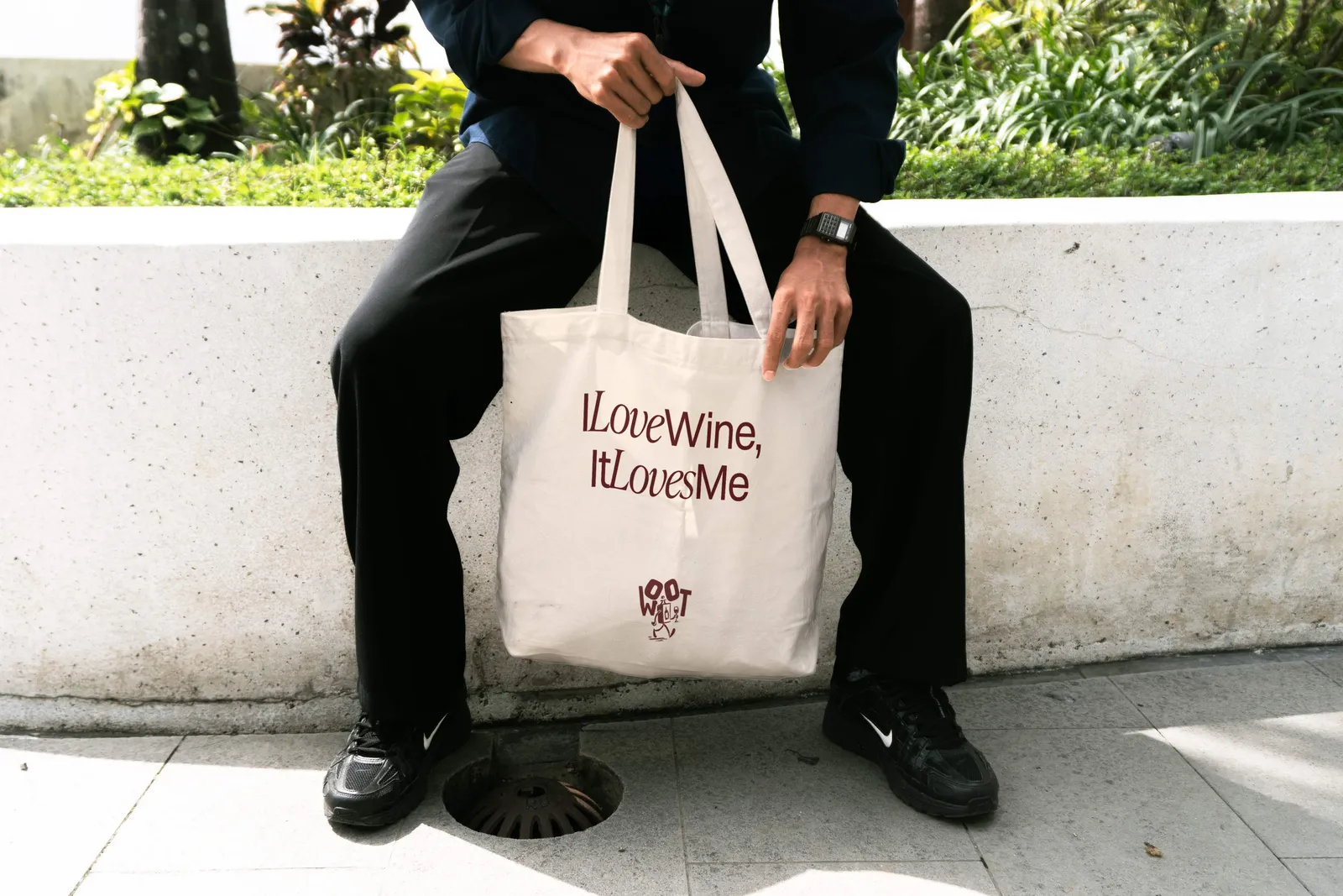 Person holding a WOOT canvas tote bag printed with 'I Love Wine, It Loves Me'